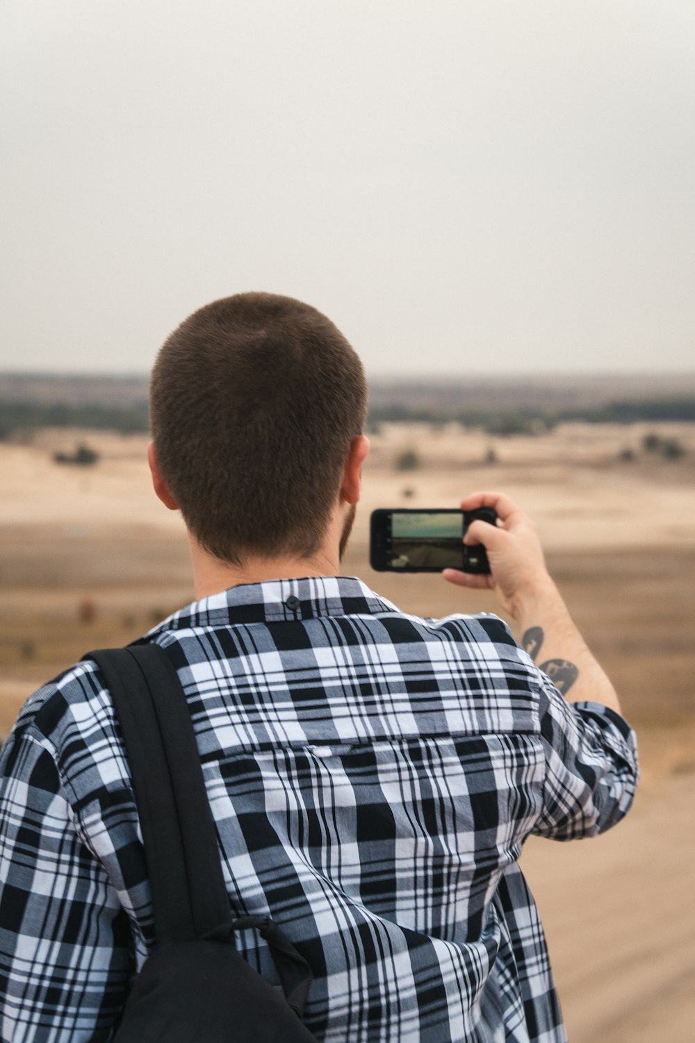 man in blue white and red plaid shirt holding black smartphone