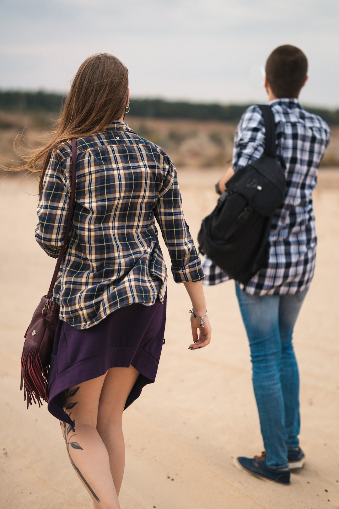 woman in black and white plaid dress shirt and blue denim shorts walking on brown sand