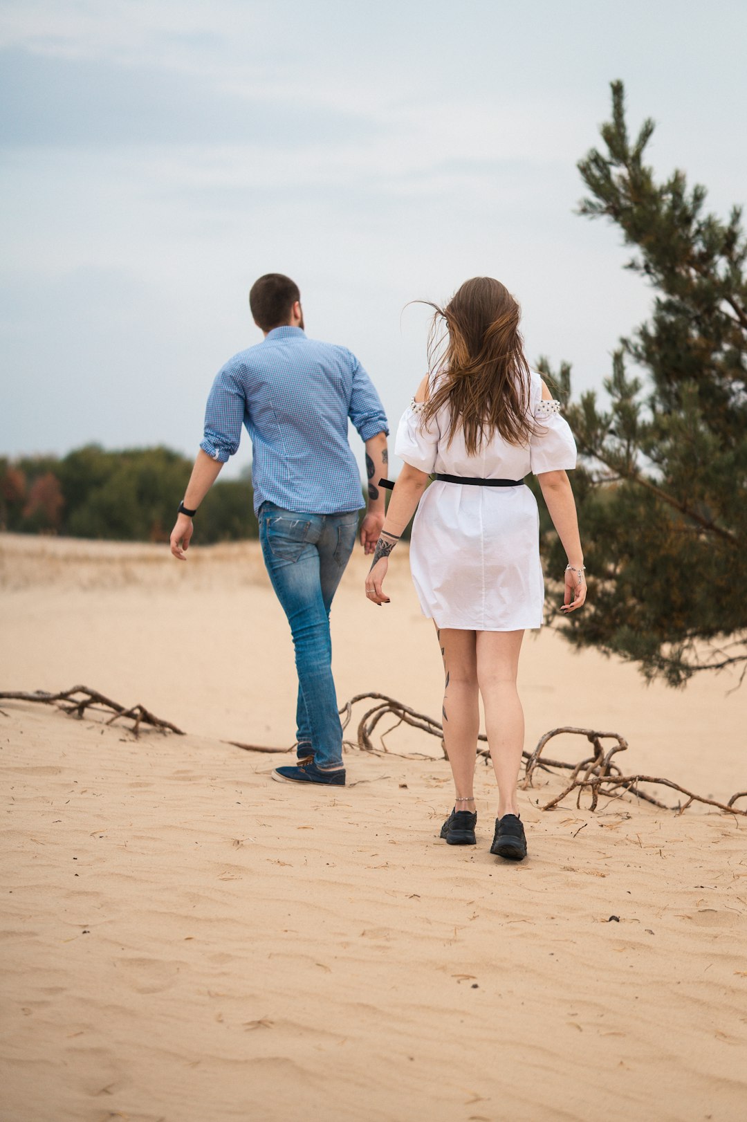man and woman holding hands while walking on sand during daytime
