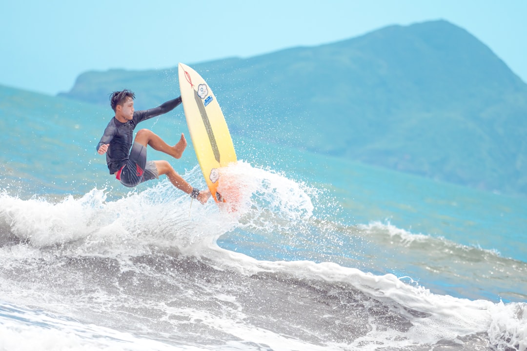 man in blue and black wet suit surfing on sea waves during daytime