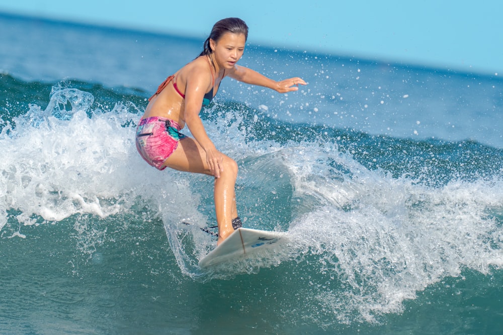 woman in pink bikini on white surfboard on sea waves during daytime