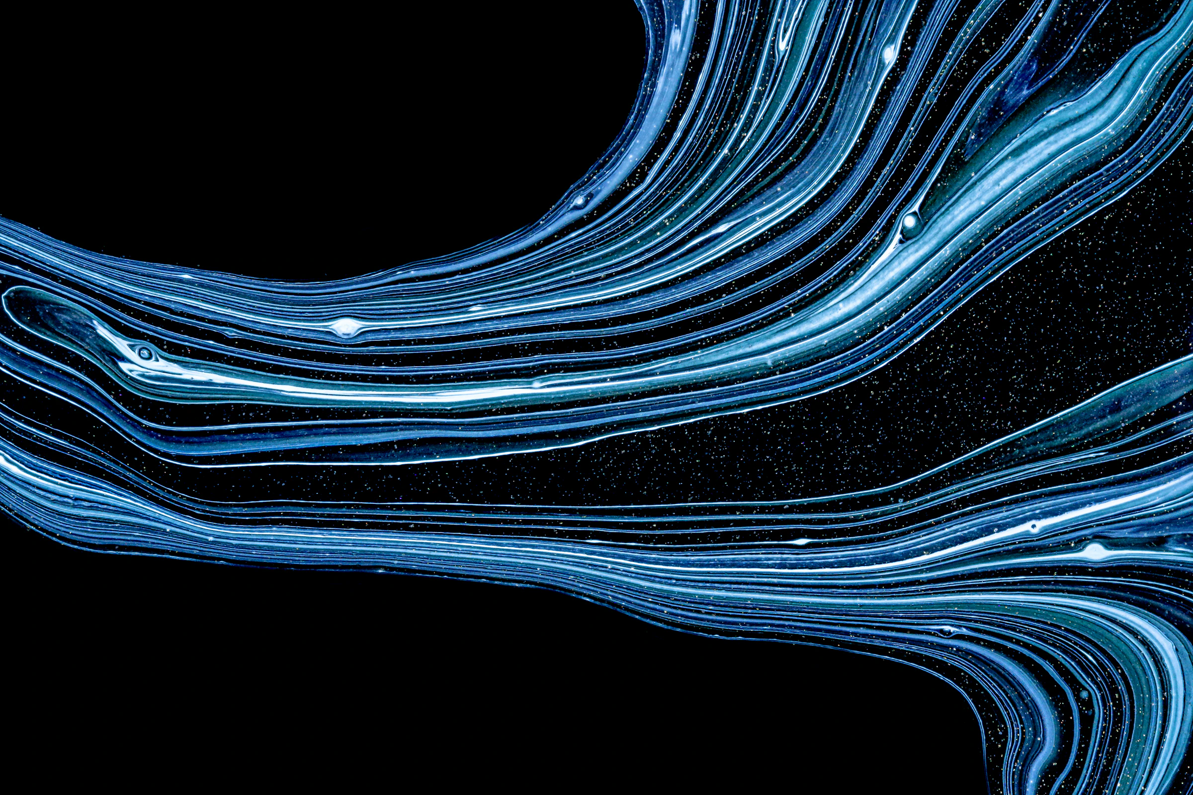 Abstract macro of swirling light blue and white liquid paint lines against a black background