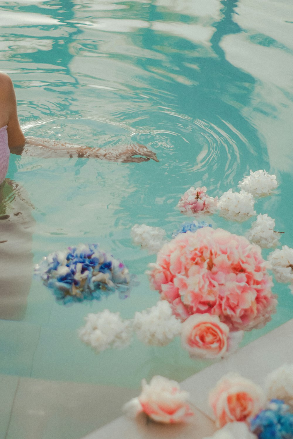 mulher no biquíni azul que nada na piscina com flores cor-de-rosa