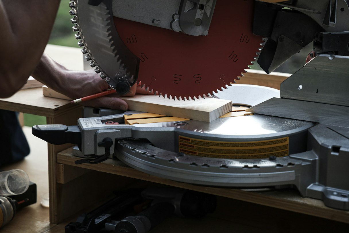 A woodworker cutting a plywood panel with a circular saw along a straightedge guide on sawhorses in a garage workshop, wearing safety glasses, wood shavings on the floor