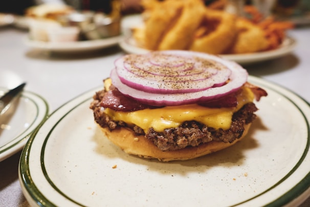 A delicious homemade burger stacked high with bacon, cheese, and fresh toppings on a white plate