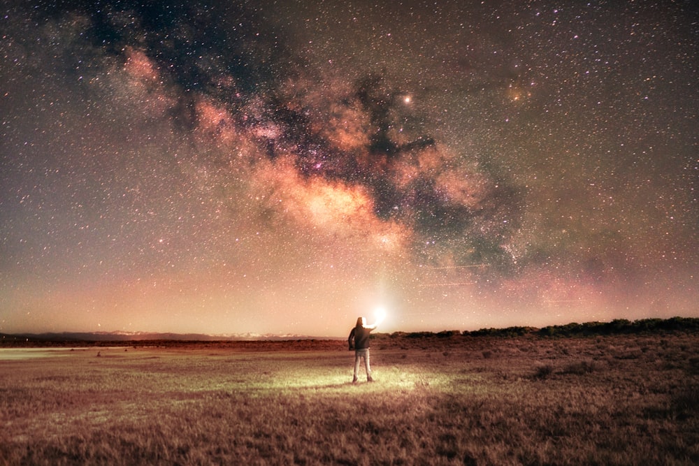 man in white shirt standing on brown grass field under starry night