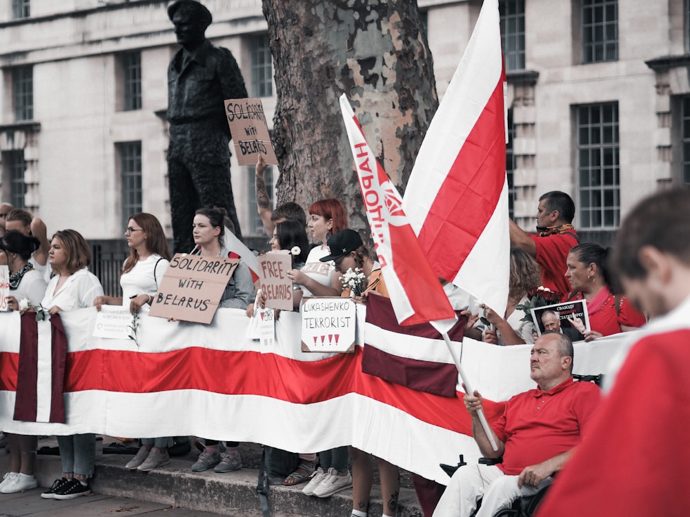 people sitting on concrete bench holding flags during daytime