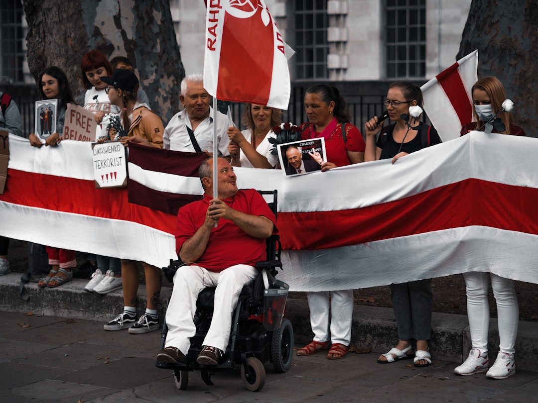 man in brown coat and white pants sitting on black wheel chair holding red and white