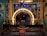 An elaborate makeup station with a large illuminated circular mirror in the center, surrounded by a golden frame. A single ornate chair sits in front of the station. Photographs and decorative wigs are displayed on either side. Teal walls and elegant carpet flooring complement the luxurious setting.