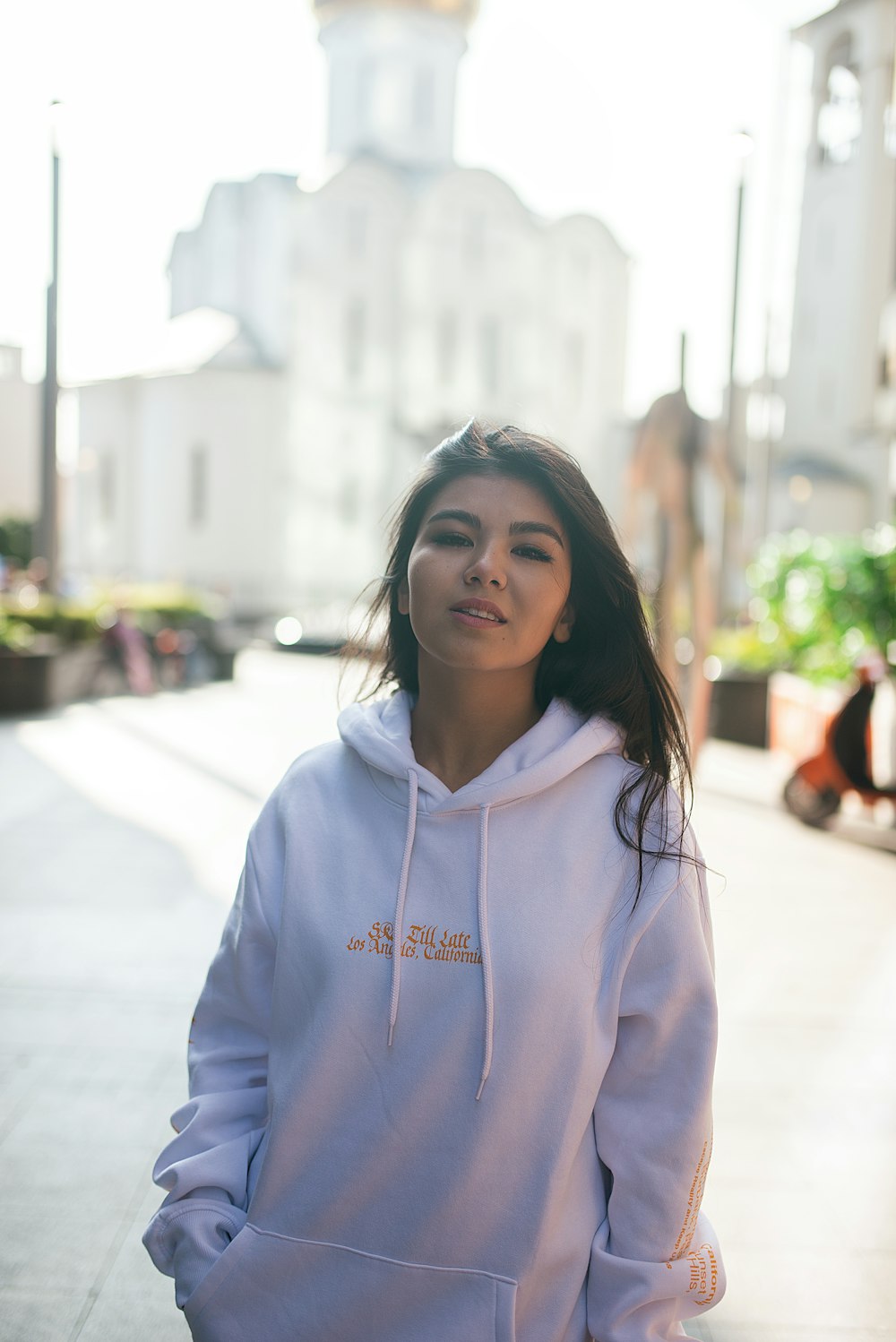 woman in white hoodie standing on street during daytime