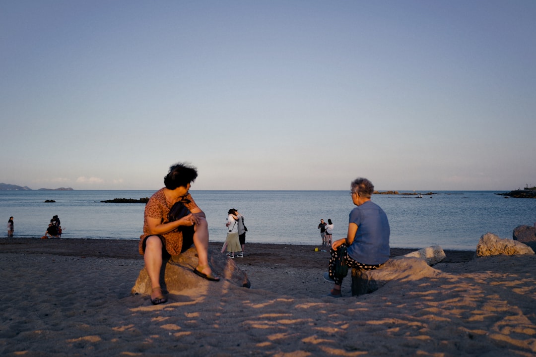 2 women and man sitting on beach shore during daytime