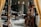 A cluttered workshop or studio filled with various objects, including wooden furniture, shelves with ceramics, art supplies, and a wooden easel. The lighting is soft, and the room has a cozy, lived-in feel.