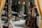 A cluttered workshop or studio filled with various objects, including wooden furniture, shelves with ceramics, art supplies, and a wooden easel. The lighting is soft, and the room has a cozy, lived-in feel.