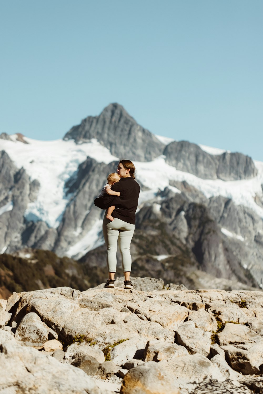 woman in black long sleeve shirt and white pants standing on brown rock formation during daytime