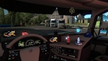 Inside the cabin of a truck, a detailed dashboard is visible with multiple controls and screens displaying maps and vehicle information. Ornamental figures, including a Santa Claus figure and a winter-themed character, are placed on the dashboard along with a cap. Outside the cabin, several parked trucks and greenery are visible, indicating a truck parking or rest area.