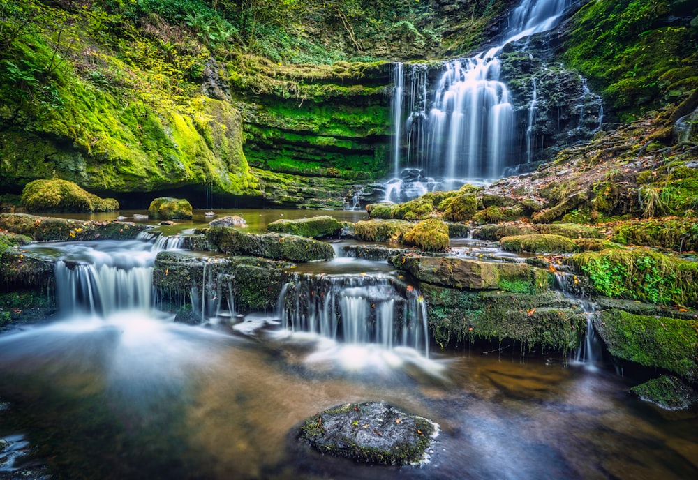 water falls in the middle of green moss covered rocks