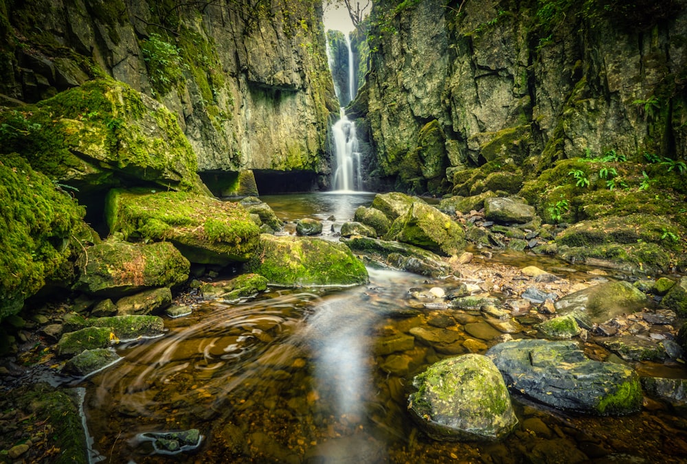 water falls between green and brown rock formation during daytime