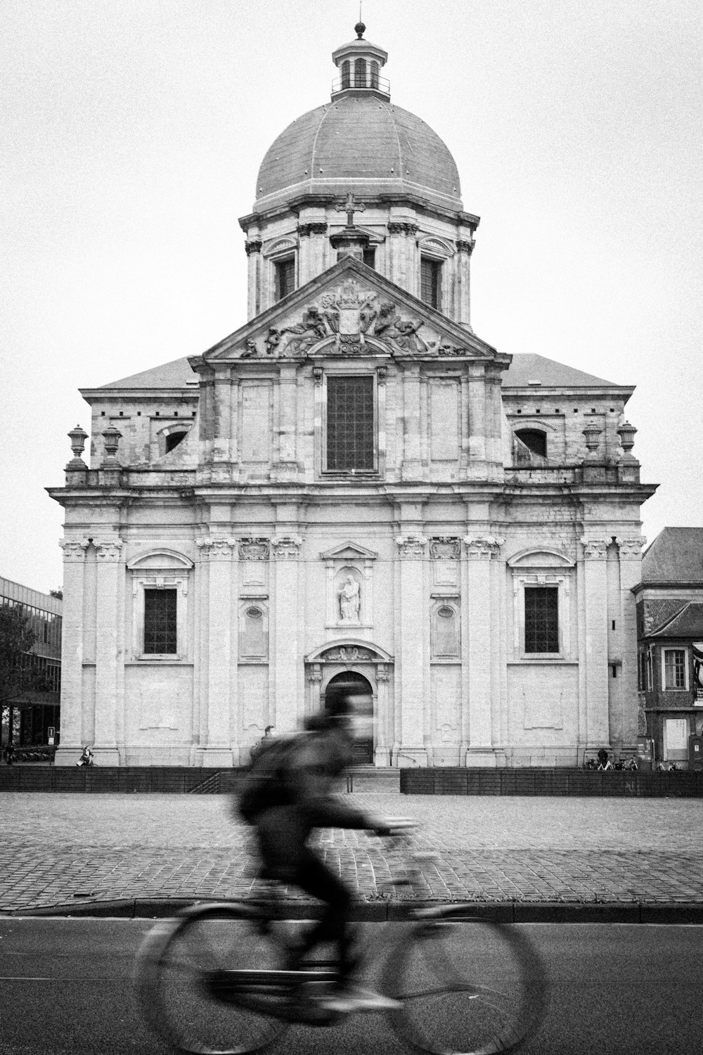 grayscale photo of man in black jacket and pants walking on sidewalk near building