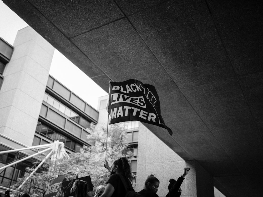 grayscale photo of man in black jacket standing near building