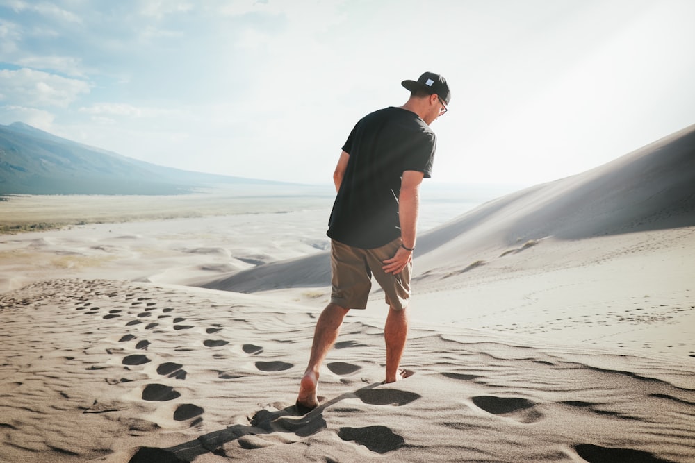 Mann in schwarzem T-Shirt und braunen Shorts tagsüber auf grauem Sand