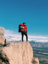 man in red and black jacket standing on brown rock formation during daytime
