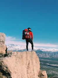 man in red and black jacket standing on brown rock formation during daytime