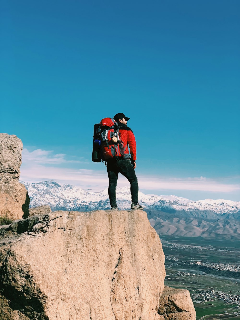 man in red and black jacket standing on brown rock formation during daytime