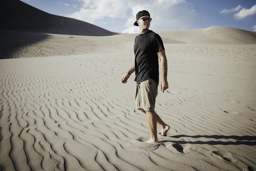 man in black crew neck t-shirt and white shorts standing on brown sand during daytime