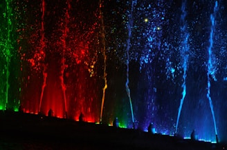 A modern water fountain with dynamic water jets illuminated by colorful lights at dusk.
