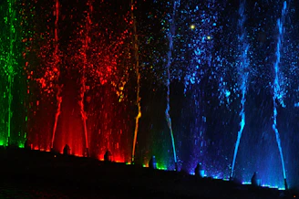 Nighttime view of the Dubai Fountain show with water jets illuminated in vibrant colors.