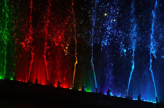 A modern water fountain with dynamic water jets illuminated by colorful lights at dusk.