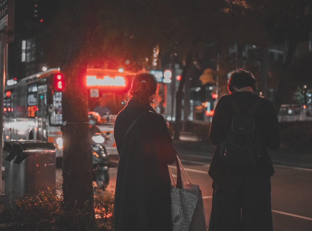 man in brown coat standing near people walking on sidewalk during night time