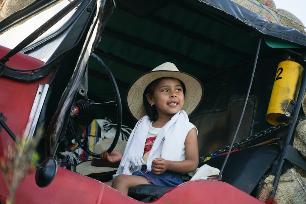 woman in white shirt and blue denim jeans wearing brown straw hat sitting on red car