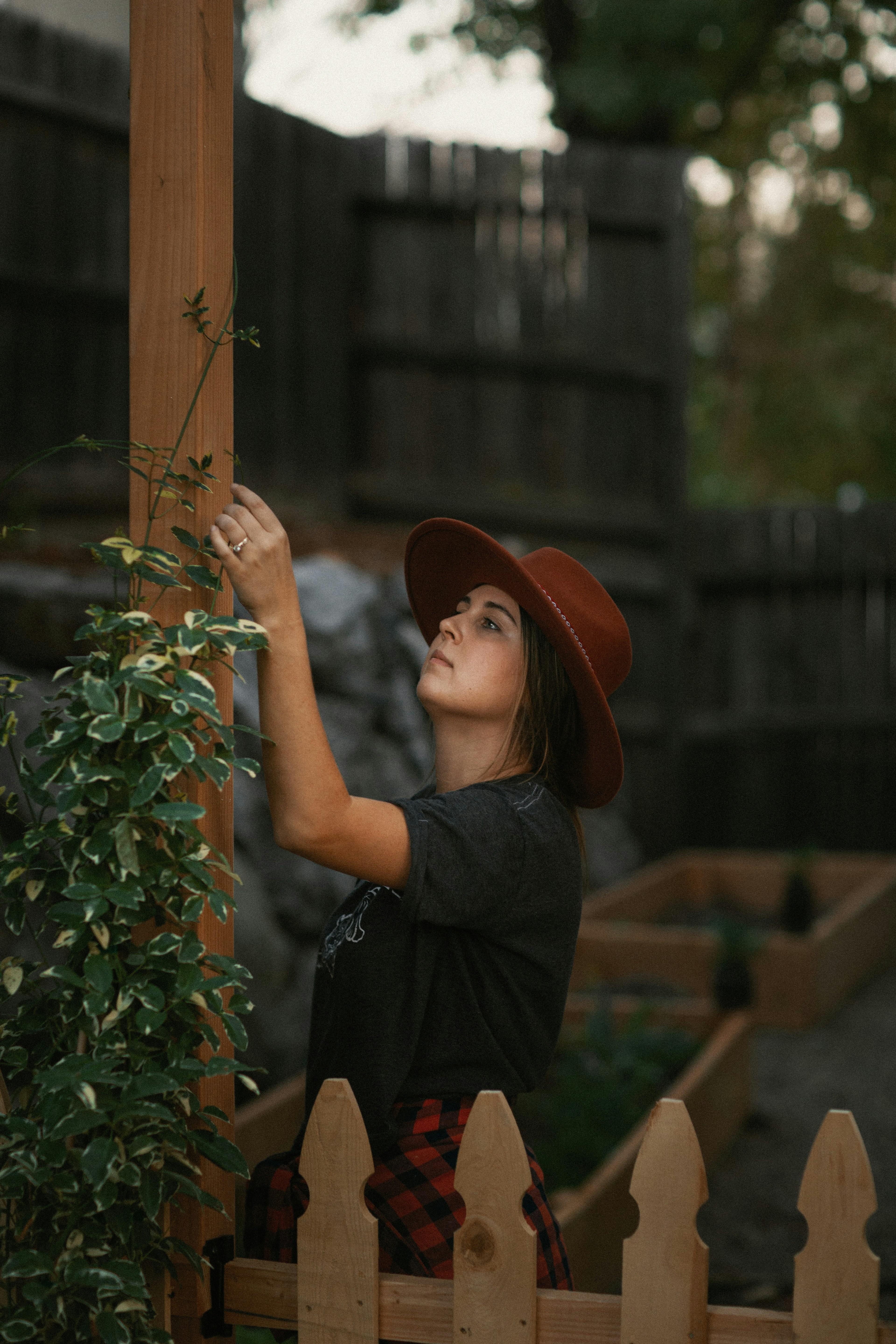 woman in black dress wearing brown fedora hat standing beside green plant during daytime