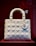 A white, quilted handbag with a structured design is displayed against a deep red background. The bag features metallic charms hanging from one of the handles, with circular rings attaching the handles to the body.