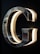 A chrome or metallic letter G is mounted on a dark background, with lighting on the inner edges creating a glowing effect. The reflective surface of the letter captures hints of the surroundings.