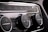 Close-up of a car's climate control panel featuring two large knobs with embedded display screens and smaller buttons for various functions. The surfaces are glossy with metallic and black elements.