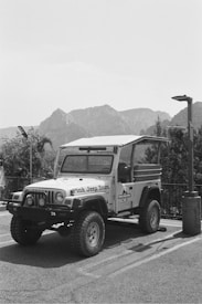 A rugged off-road vehicle with the words 'Pink Jeep Tours' on its side is parked in an outdoor setting. The background features a mountainous landscape under a clear sky. The environment suggests a location suitable for adventure and exploration.