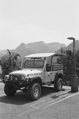A rugged off-road vehicle with the words 'Pink Jeep Tours' on its side is parked in an outdoor setting. The background features a mountainous landscape under a clear sky. The environment suggests a location suitable for adventure and exploration.