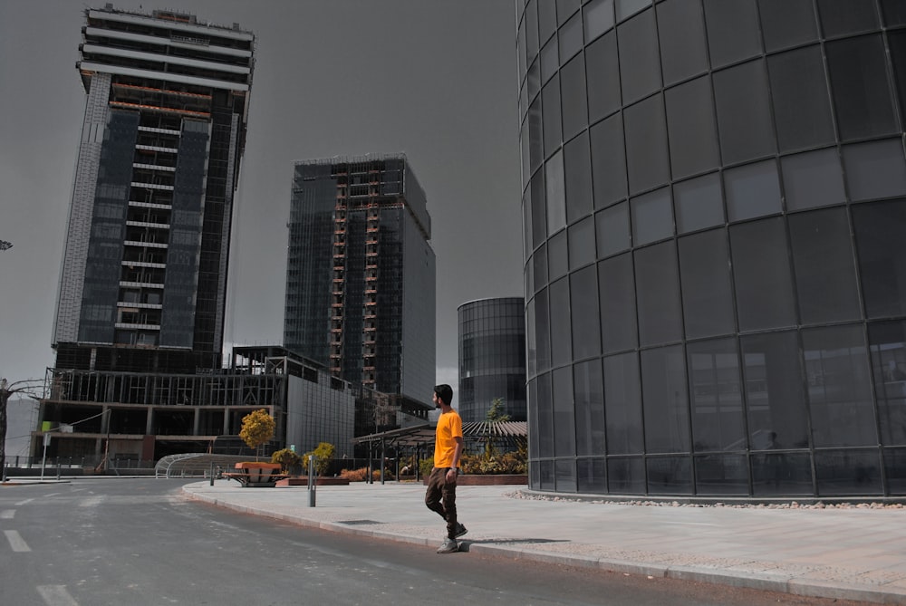 노란 재킷과 검은 바지를 입은 남자가 낮 동안 고층 건물 근처 보도를 걷고 있다