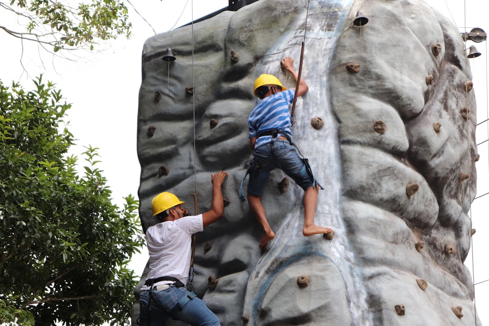 2 men climbing on gray rock during daytime