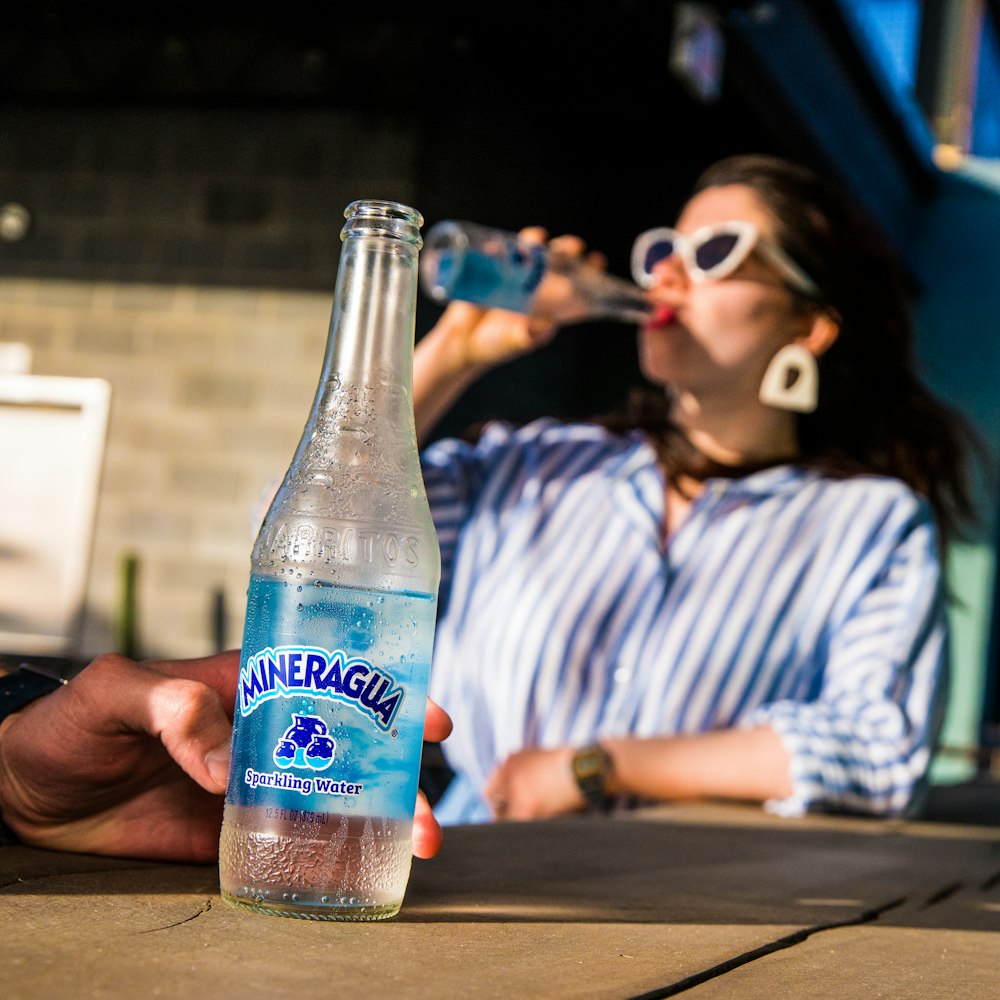 Femme en chemise à rayures bleues et blanches tenant une bouteille étiquetée bleue