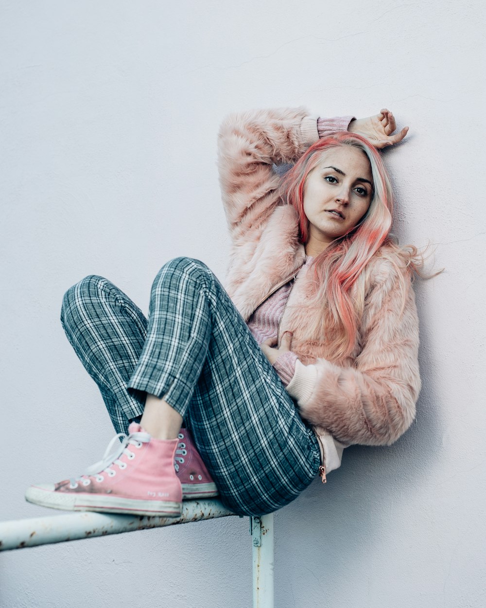 woman in beige fur coat and black and white plaid pants sitting on white floor