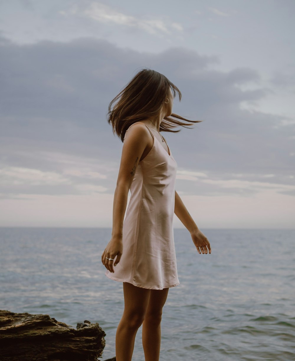 Frau in weißem Kleid, die tagsüber auf einem Felsen in der Nähe des Meeres steht