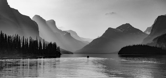 grayscale photo of person riding on boat on lake in Maligne Lake Canada