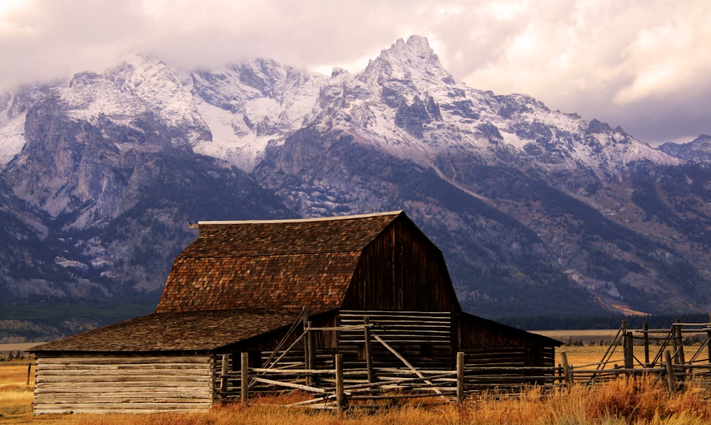 brown wooden barn near snow covered mountain during daytime