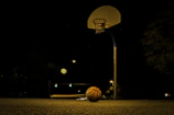 A sleek backyard basketball court glowing under custom lighting at dusk.