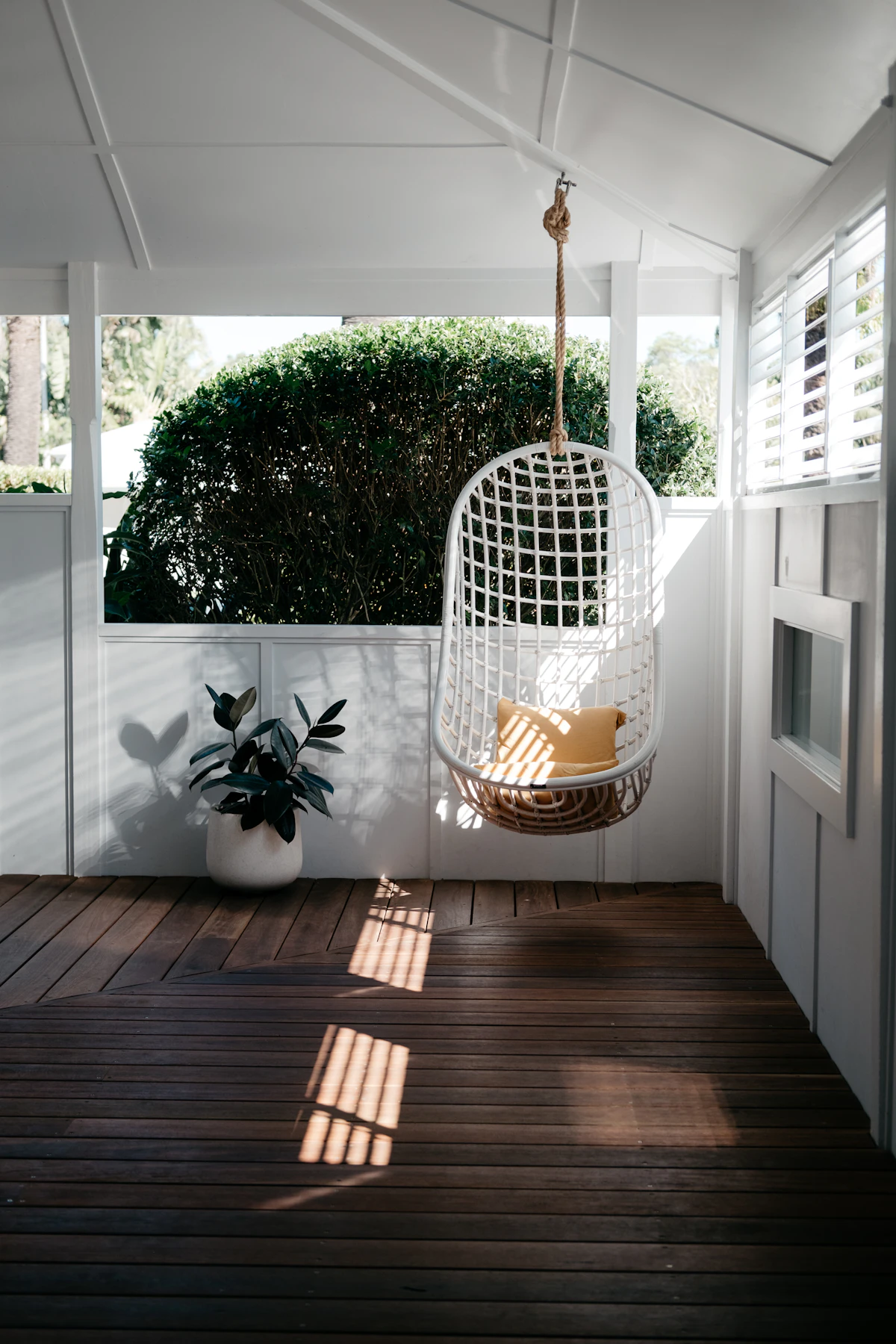 Solid teak wood swing with hand-carved detailing and brass chains in a sunlit veranda