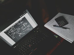A student studying math problems alone with notes and a laptop in a cozy room.