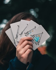 Close-up of hands holding Red Heron cards with natural greenery in the background.